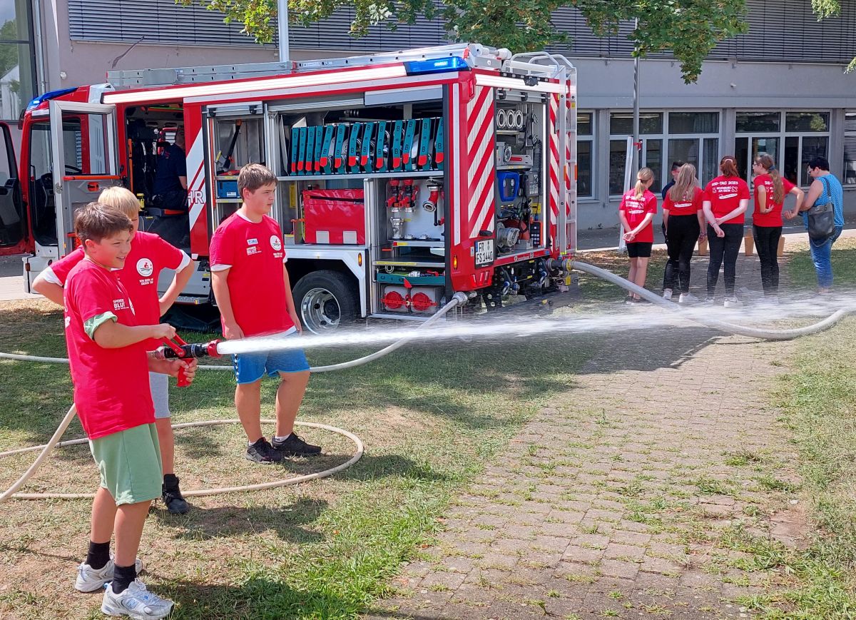 Drei Schüler mit Wasserwerfer vor einem Feuerwehrwagen